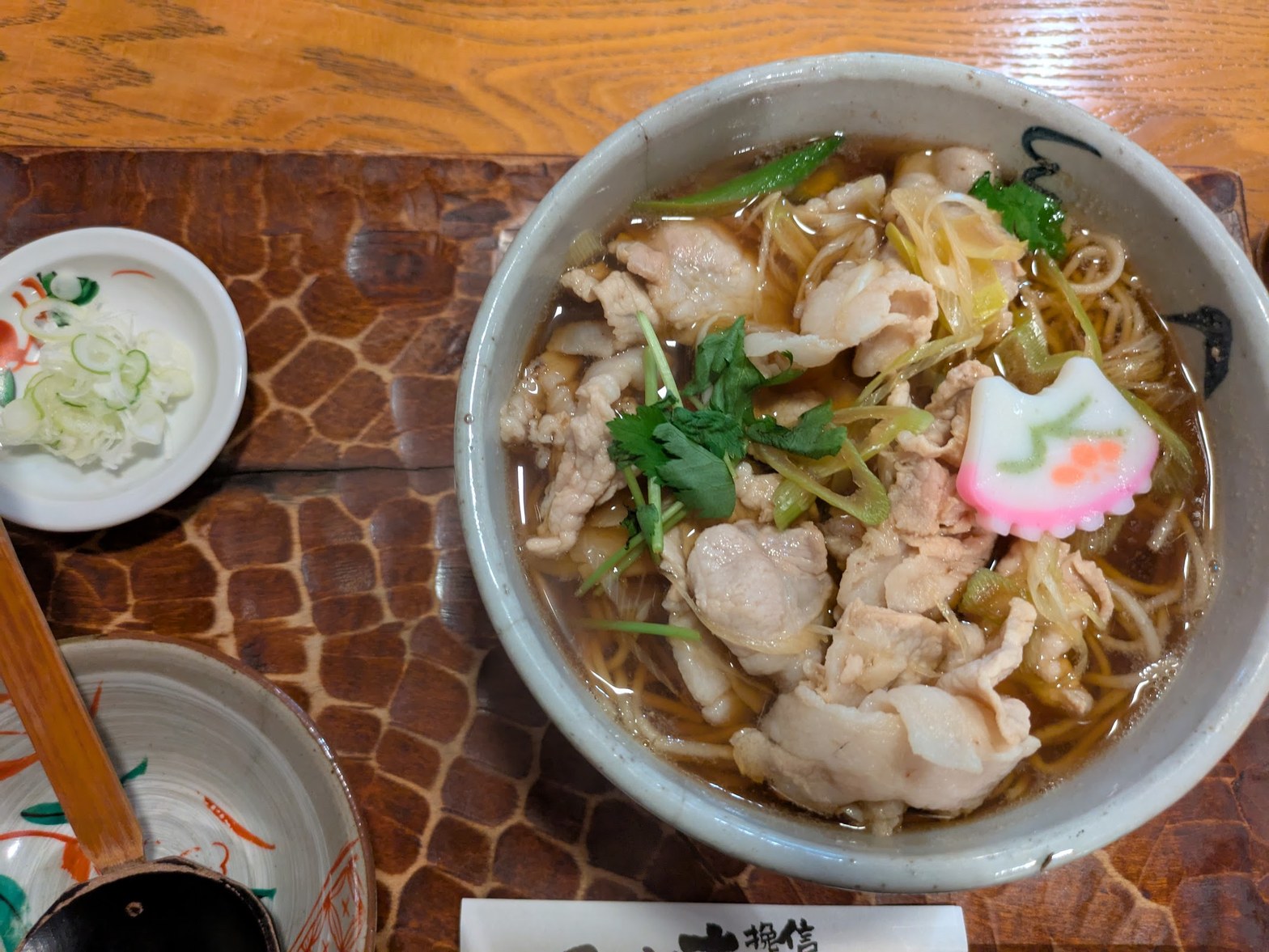 大きな陶器鉢に鶏肉・ネギ・三つ葉・なると入りの蕎麦が盛られた温かい麺料理