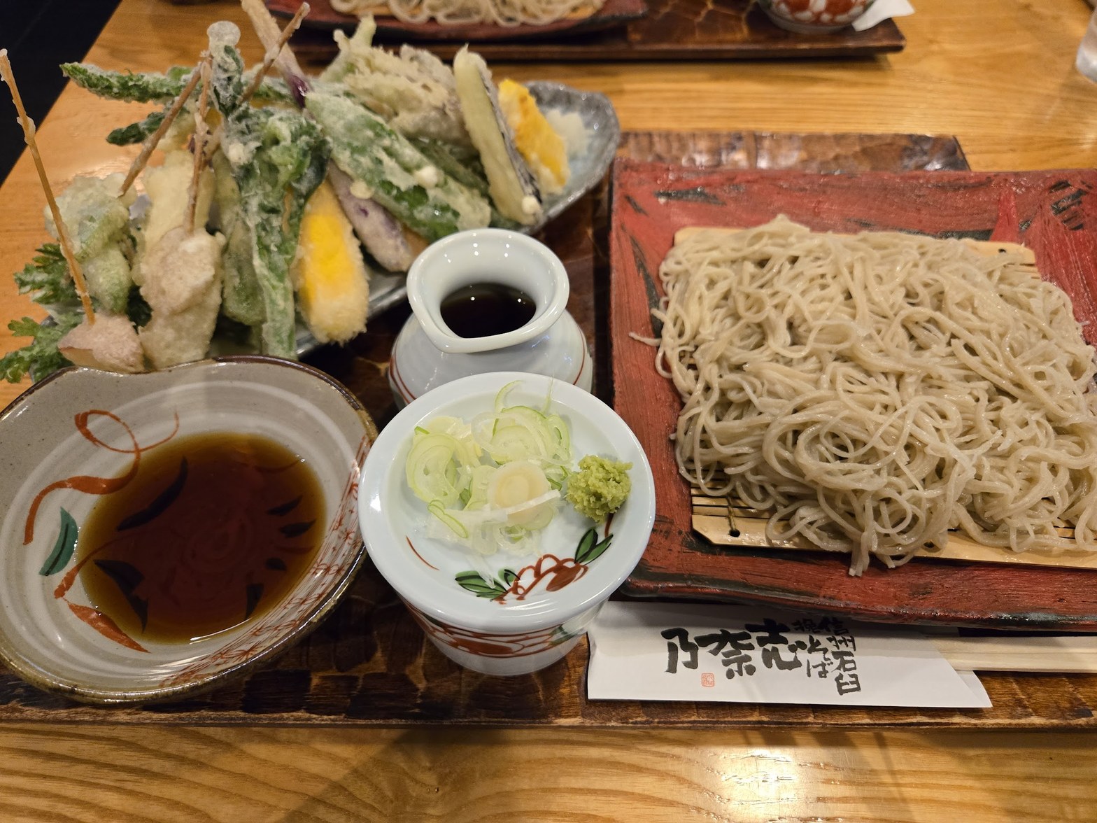 赤い角皿に盛られた蕎麦と、手前に蕎麦つゆ・薬味小皿、奥に天ぷら数種が並ぶ天もりの全景